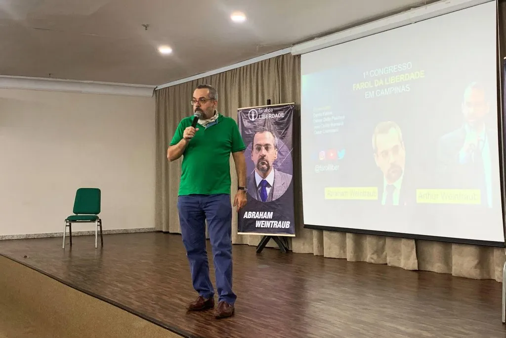 Palestrante de camisa verde fala ao microfone diante do telão do congresso de Campinas